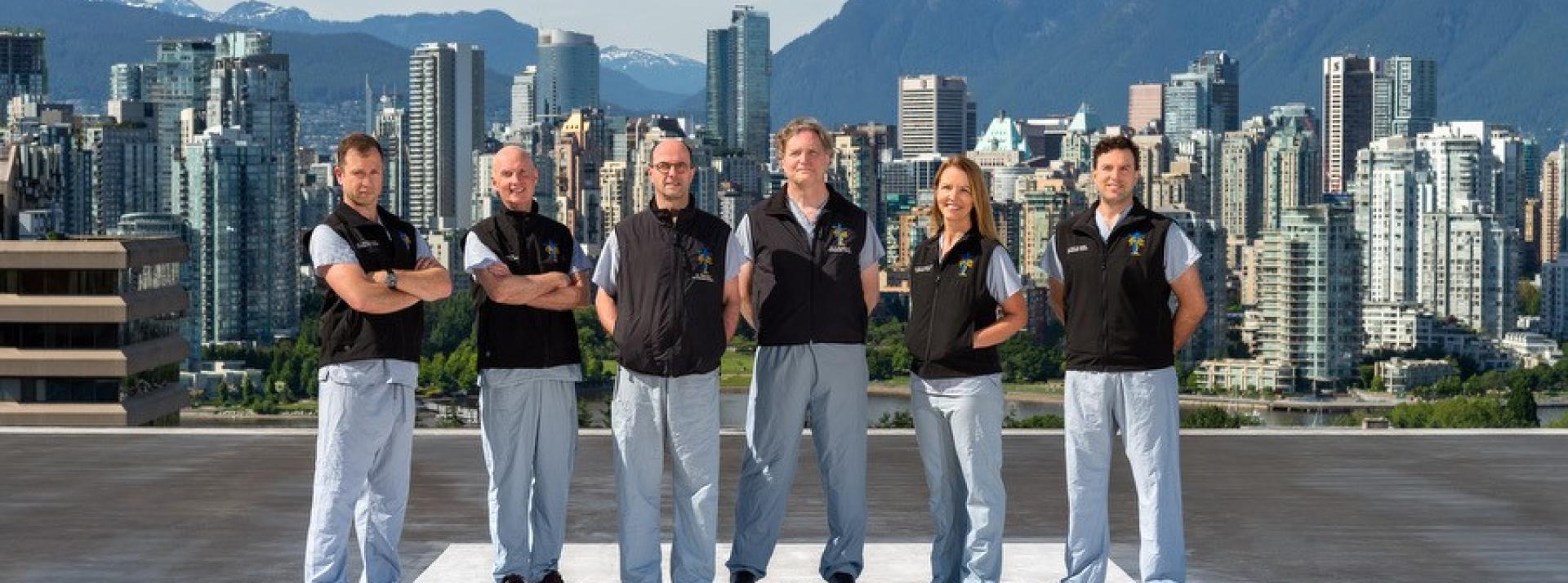 Six members of a trauma team stand on a helipad with mountains in the background.