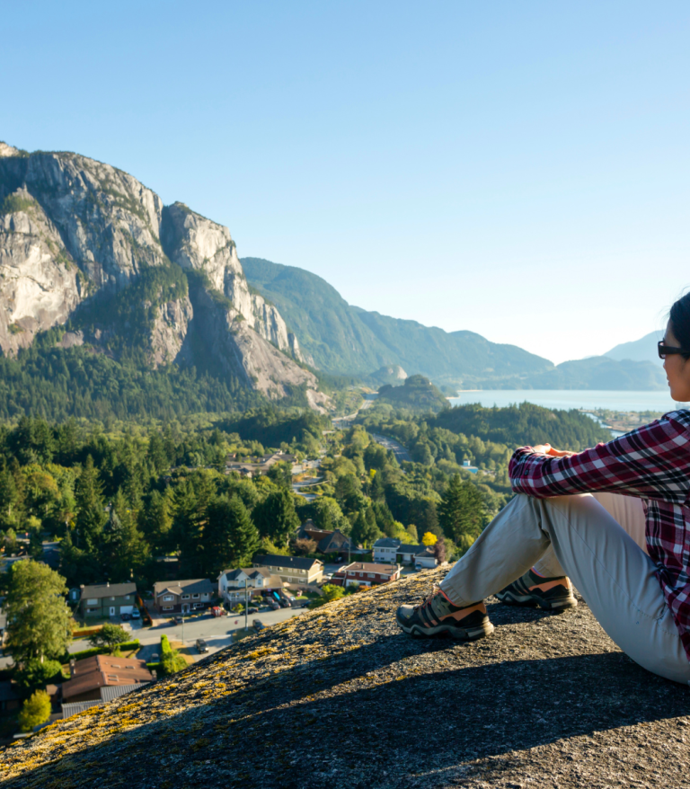 A person sitting on top of a hill looking out over Squamish, the chief is visible in the background