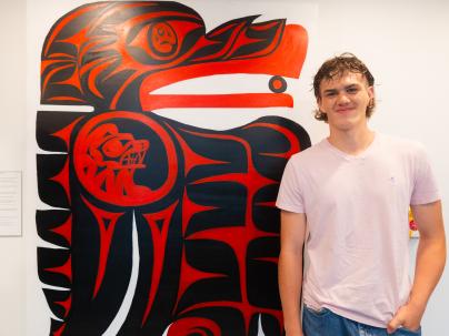 Ryan Hughes, an artist from Snuneymuxw First Nation, standing in front of his artwork.