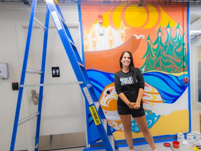 Diamond Point, an artist and member of the Musqueam Nation, standing in front of her mural at the Downtown Eastside Youth Outreach space.