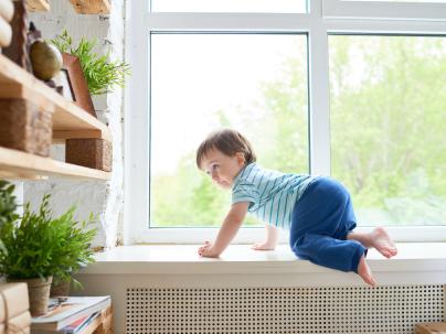 A little boy climbs up on window ledge