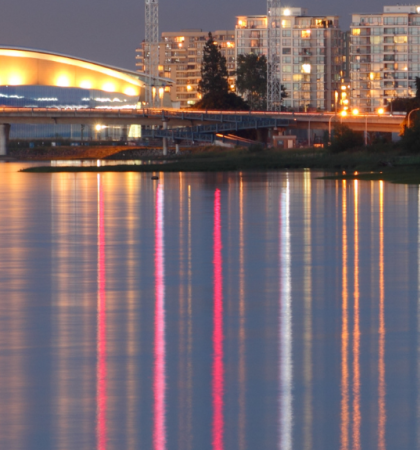Richmond Olympic Oval lit up in background with river in front of the photo.
